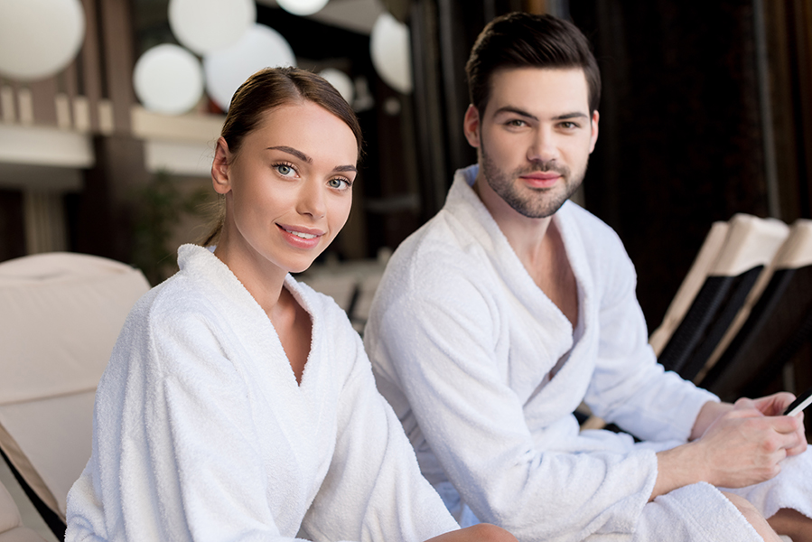 beautiful young couple in bathrobes smiling at camera in spa cen